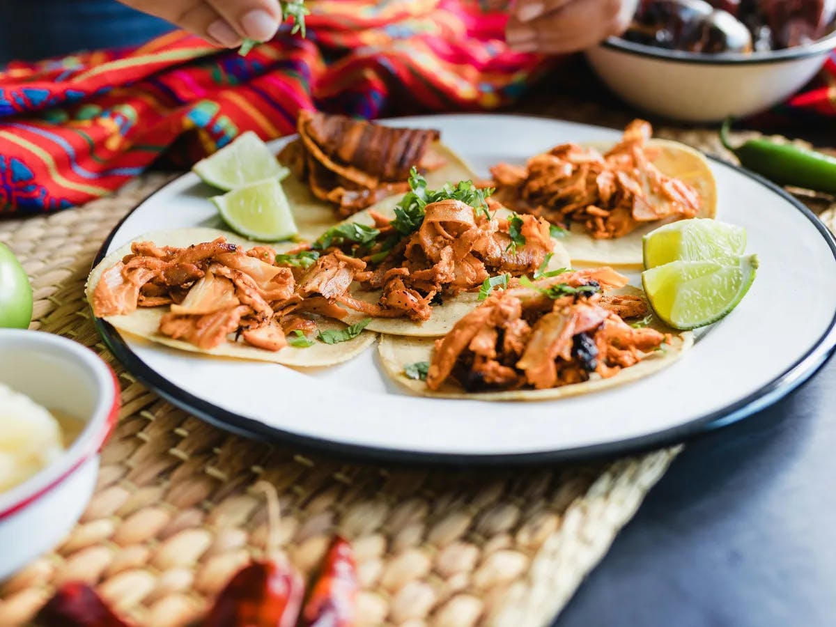 The image shows a plate of three tacos with a garnish on top, accompanied by lime wedges.