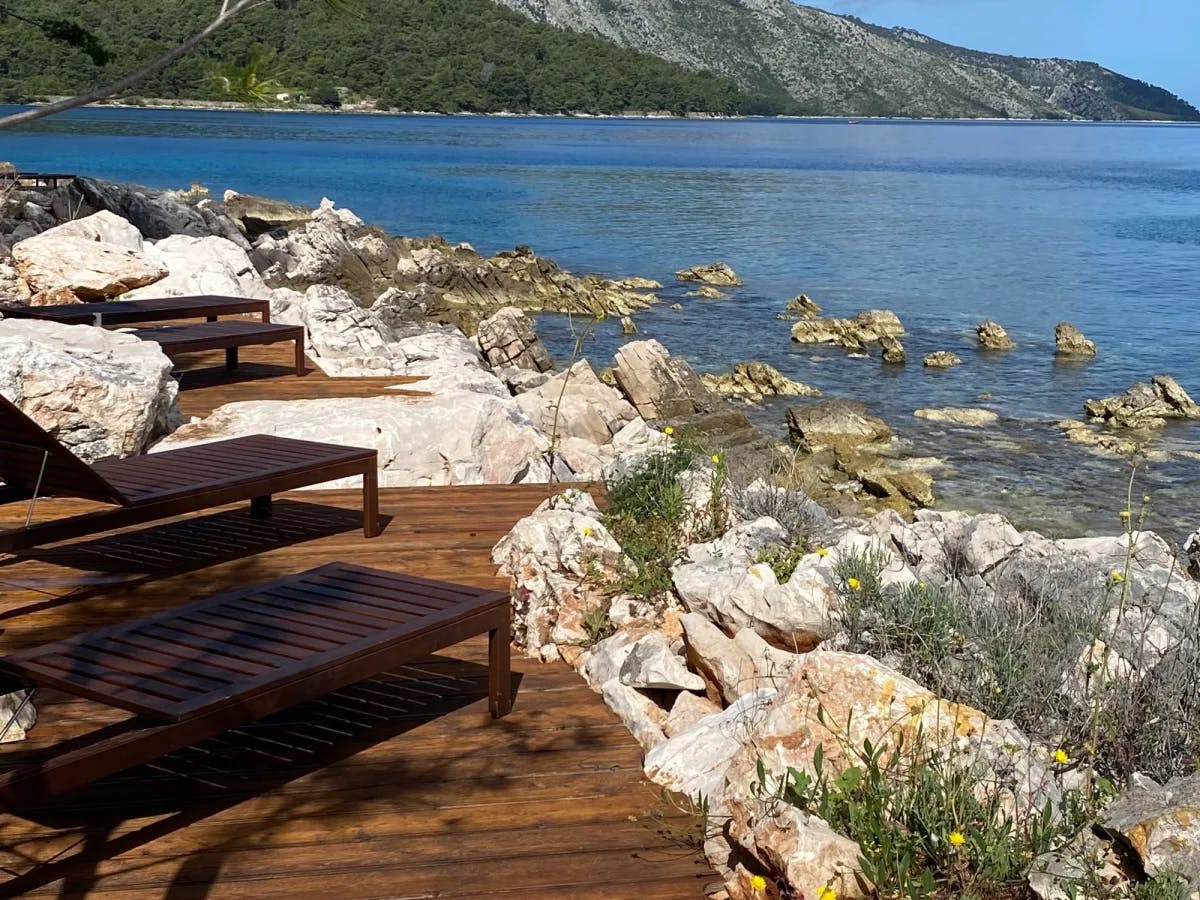 A wooden deck with benches facing the sea with a rocky shoreline on a sunny day.