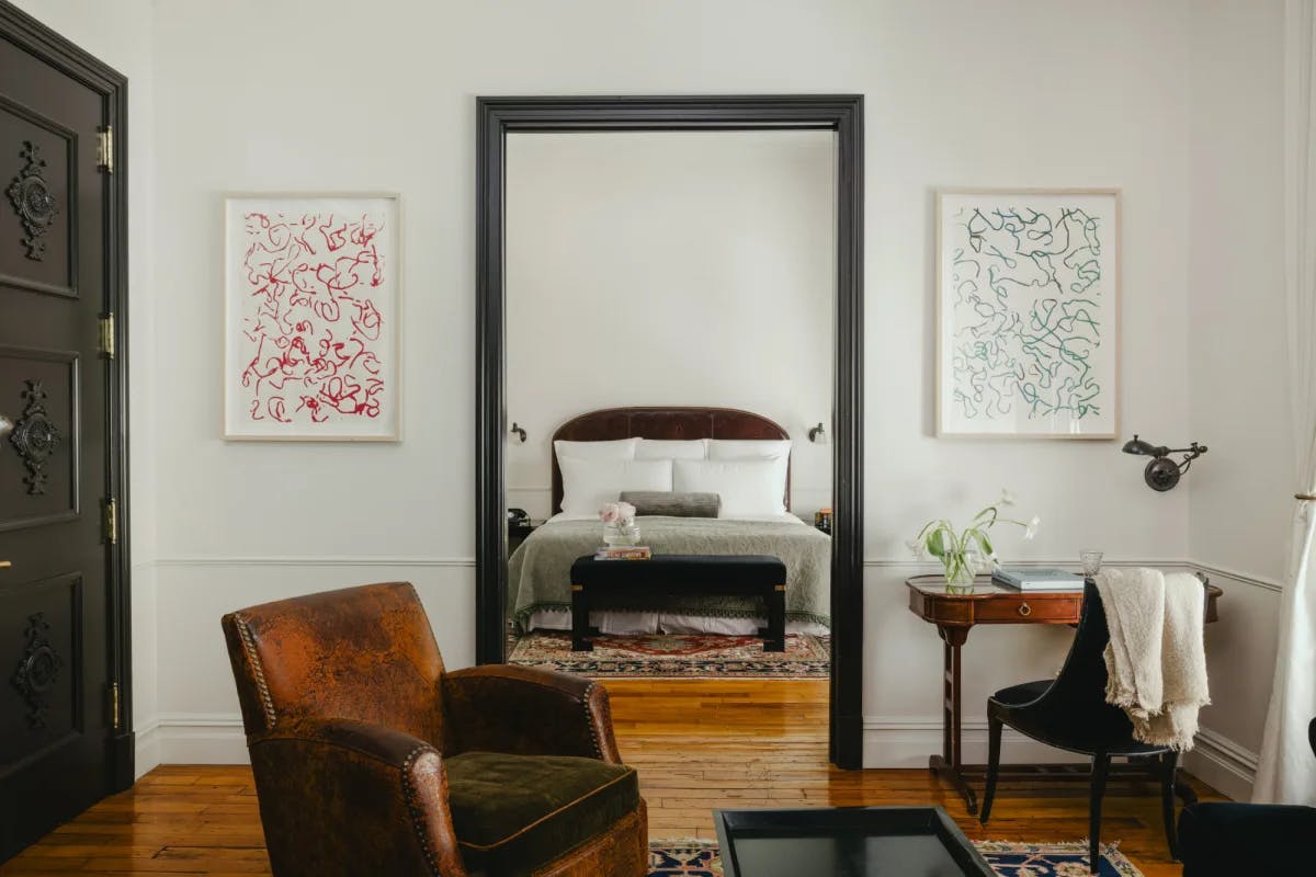 a handsome hotel room with a leather chair in a living room that looks into a separate bedroom