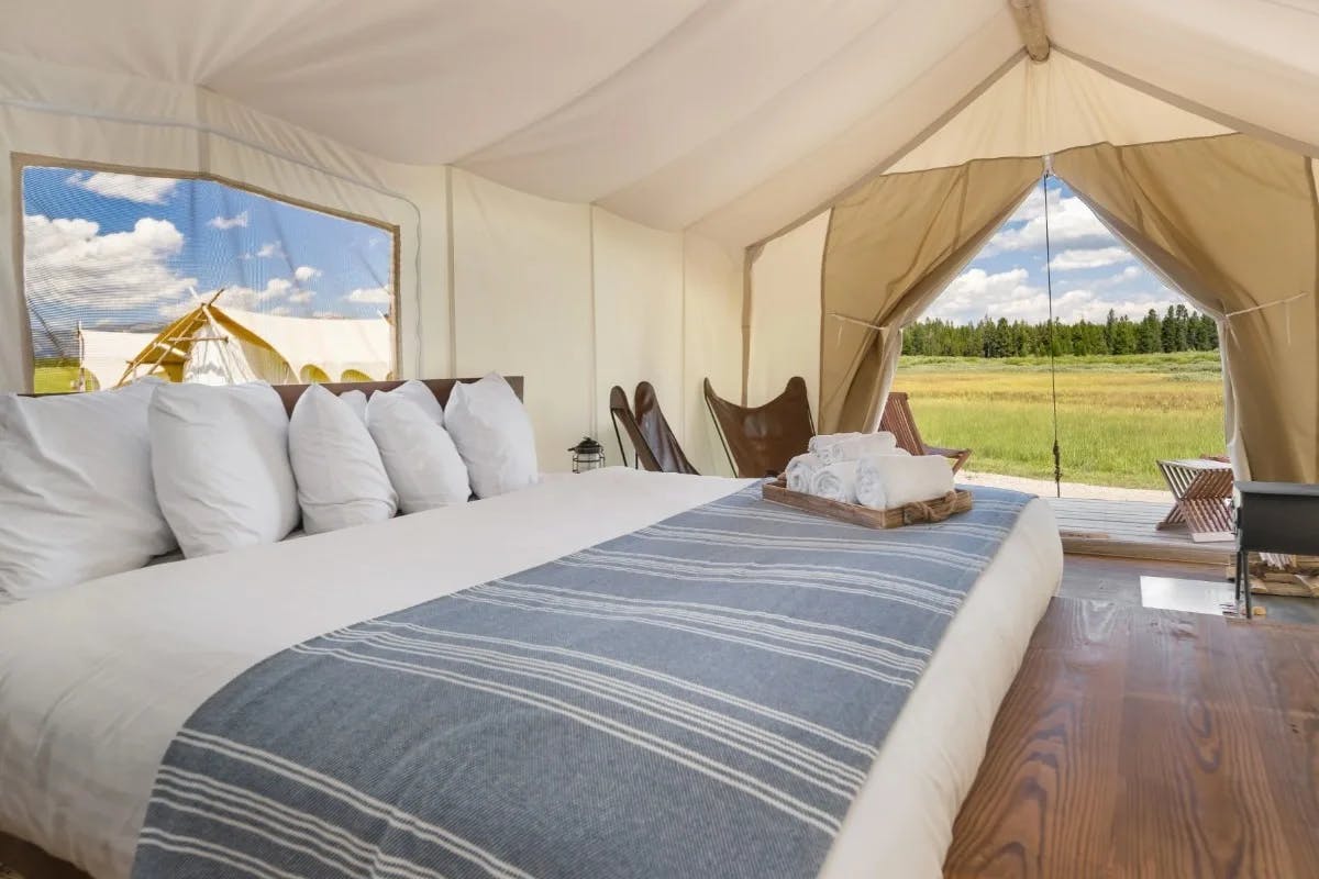 canvas tent with large bed and a view to a mountain meadow