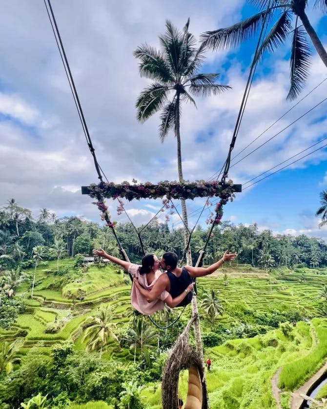 Travel advisor Cortney posing on a swing kissing male companion high above a lush forest