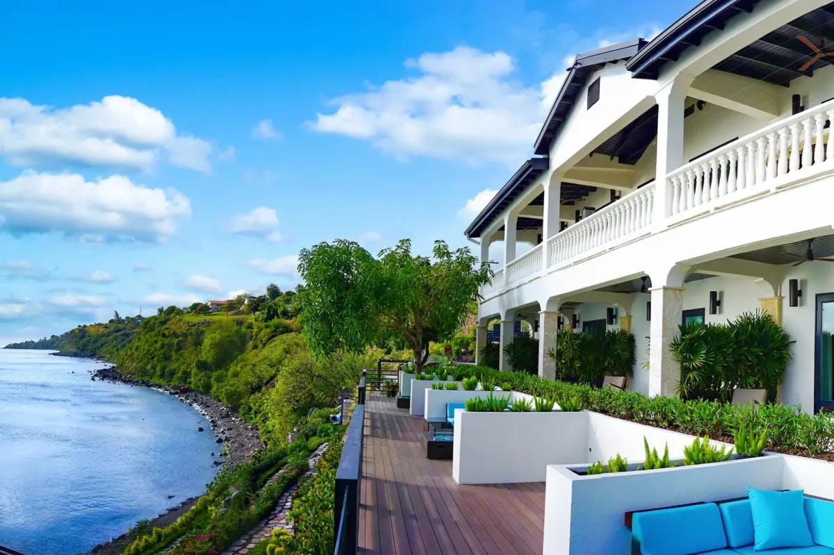 A lounge area and resort overlook a stone path and rocky beach on the shores of Saint Kitts