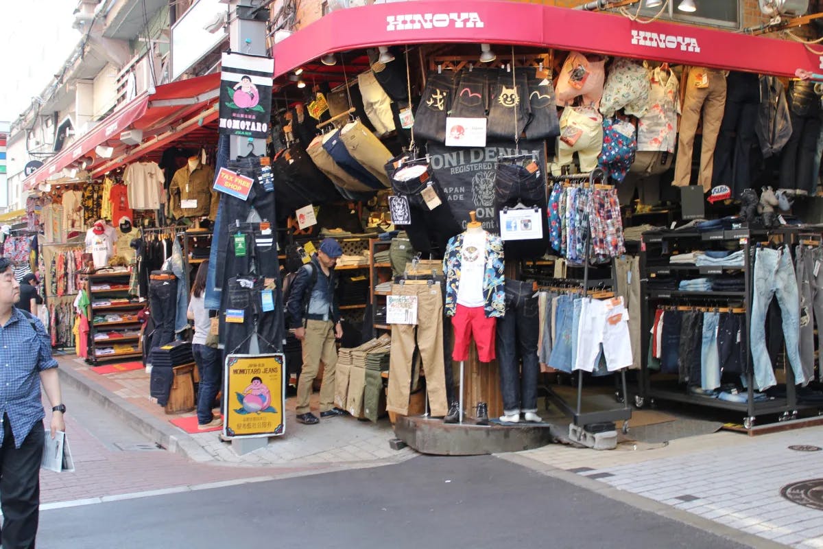 A street corner with clothing hung up for sale beneath a red awning that reads "Hinoya". 