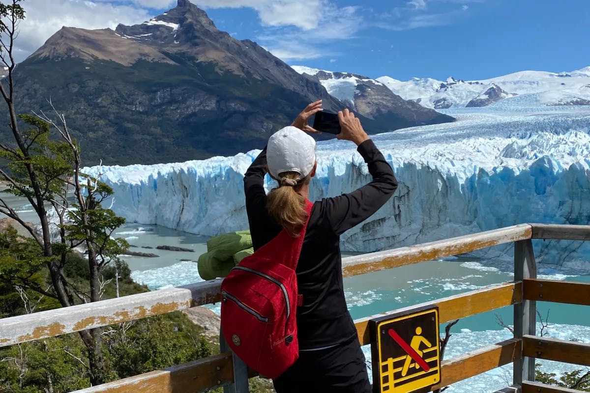 A woman taking a photo of a glacier from a wooden deck.