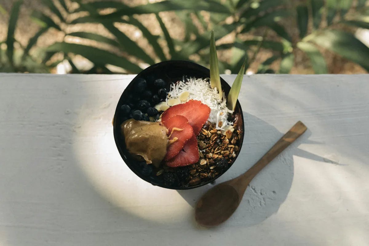 An acai bowl on a white table with palm fronds in the background.