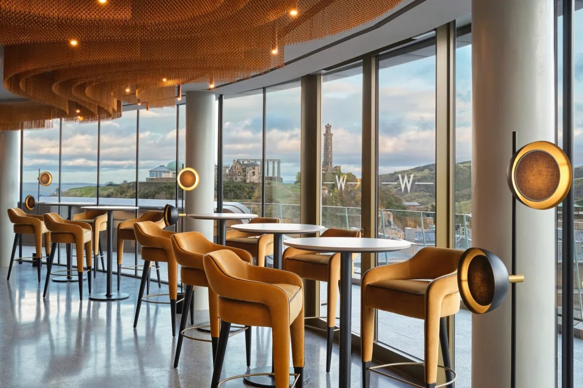 A view of a bar area at W Edinburgh with high bar chairs and small round tables, with a view of the city of Edinburgh