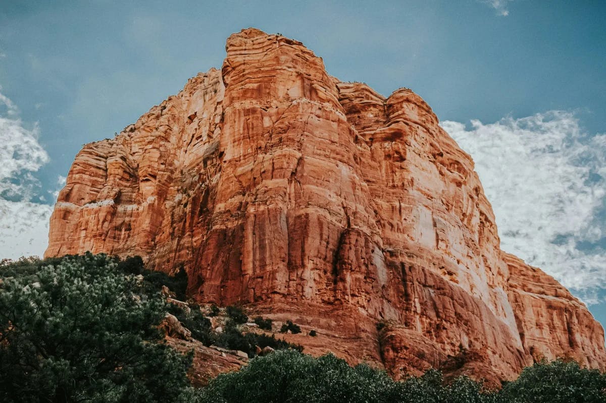 A craggy mountain stands tall against a blue sky dotted with clouds. 