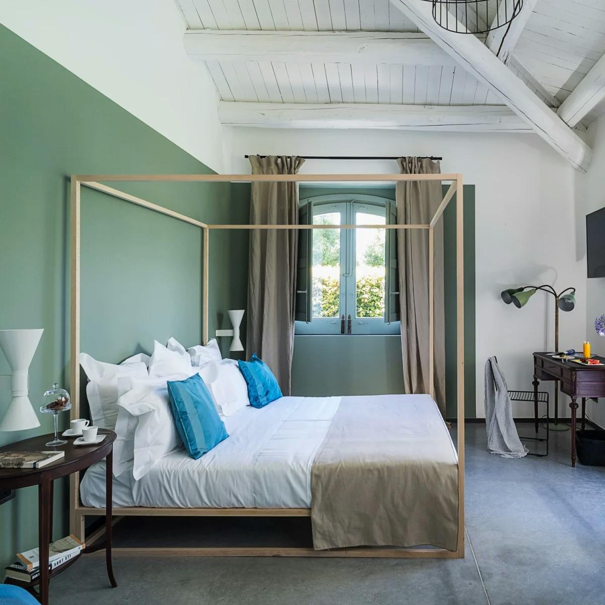 a green-walled, sunny bedroom with a four post bed