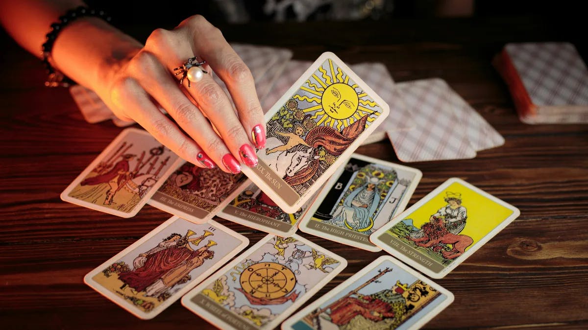 A table with tarot cards and a hand holding one up.