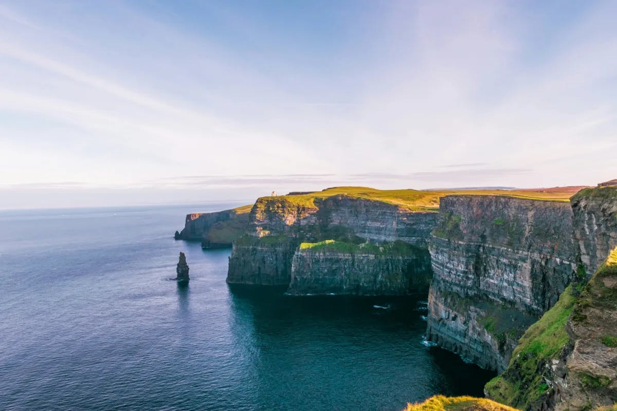 Dramatic cliffs with the sun shining onto the grassy landscape and calm ocean below