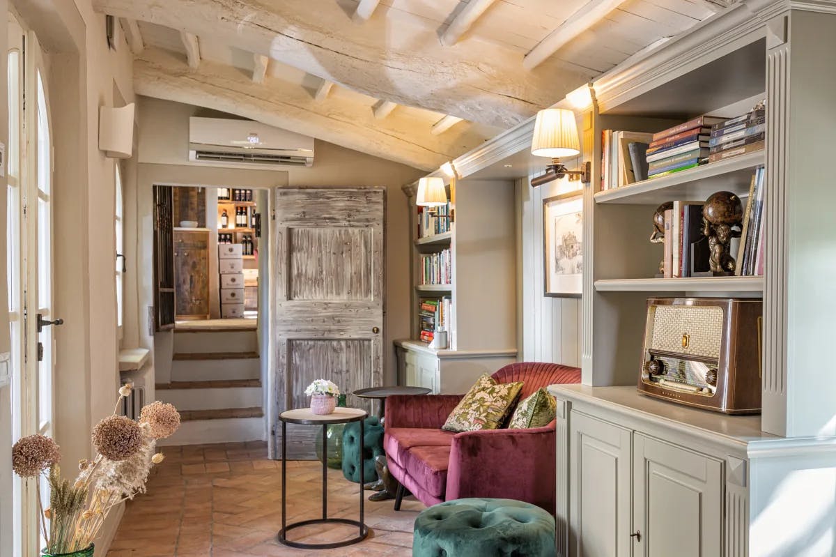 a cozy library with a pink couch, green stools and an armoire filled with books and knick-knacks