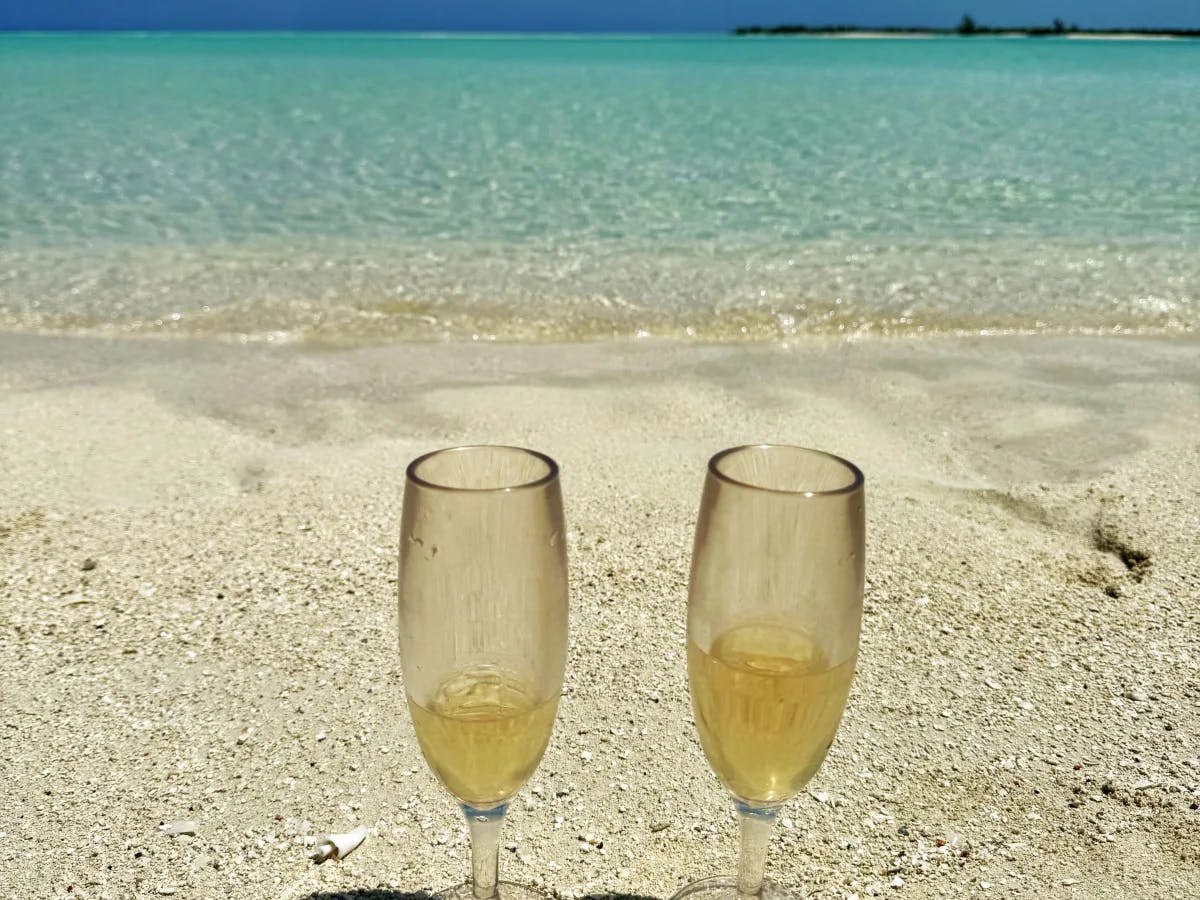 The image features two champagne glasses on a beach, symbolizing a celebratory moment against a backdrop of blue skies and turquoise waters.