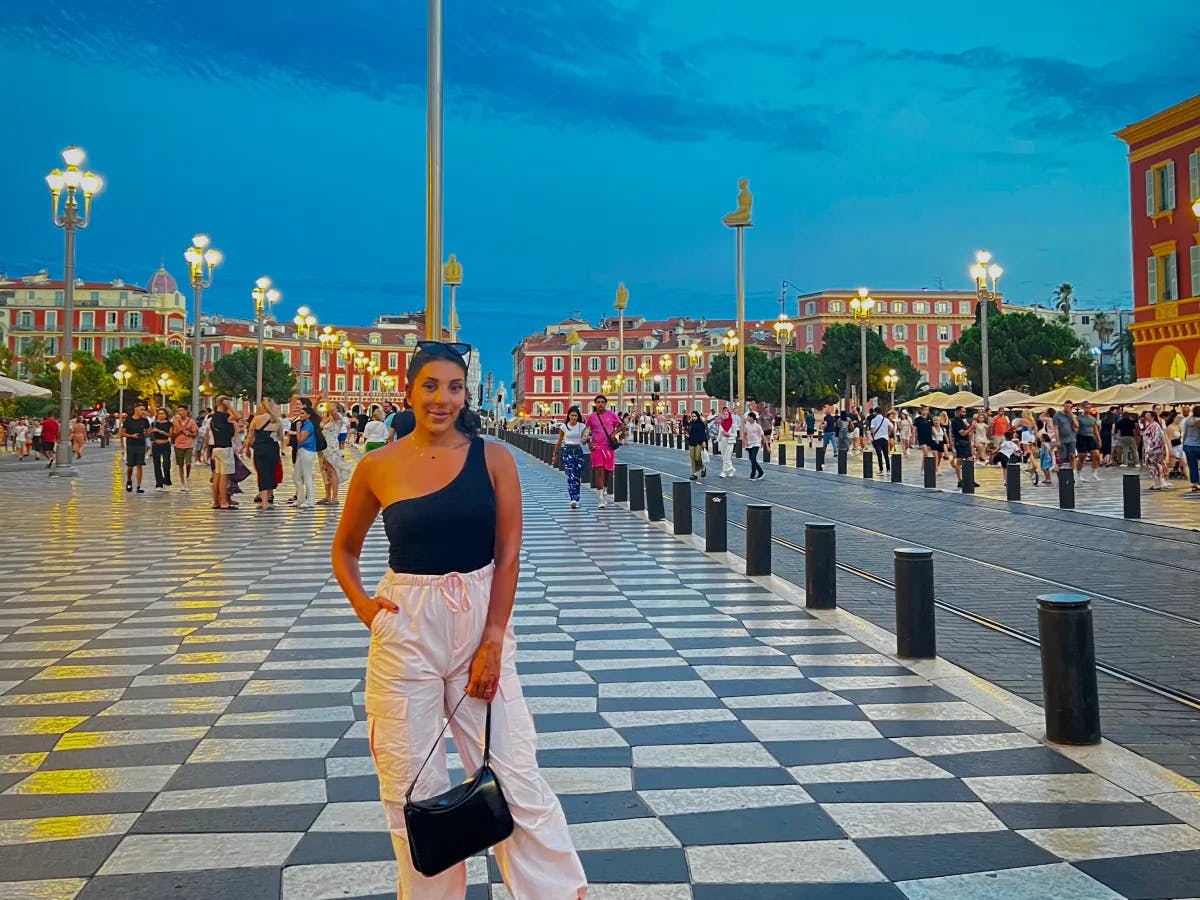 A girl standing on the checkered sidewalk at evening.