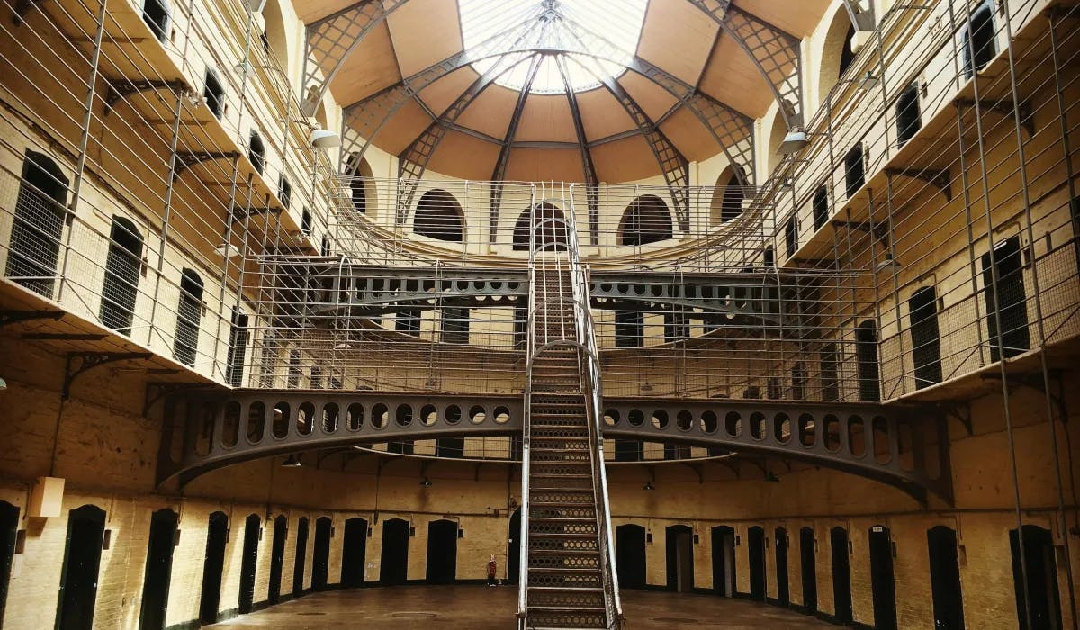 Inside Kilmainham Gaol, a historic prison in Dublin, three stories with many doors on each floor, iron gates and staircase and a domed ceiling with a skylight.