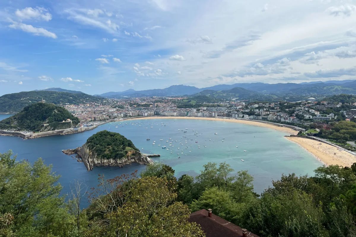 View from Monte Igueldo, with two small islands near the coastline, which is dotted with houses and trees.