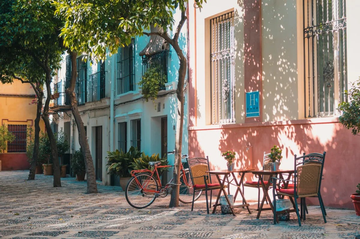 Chairs, tables and a bicycle outside cute pink and blue buildings.