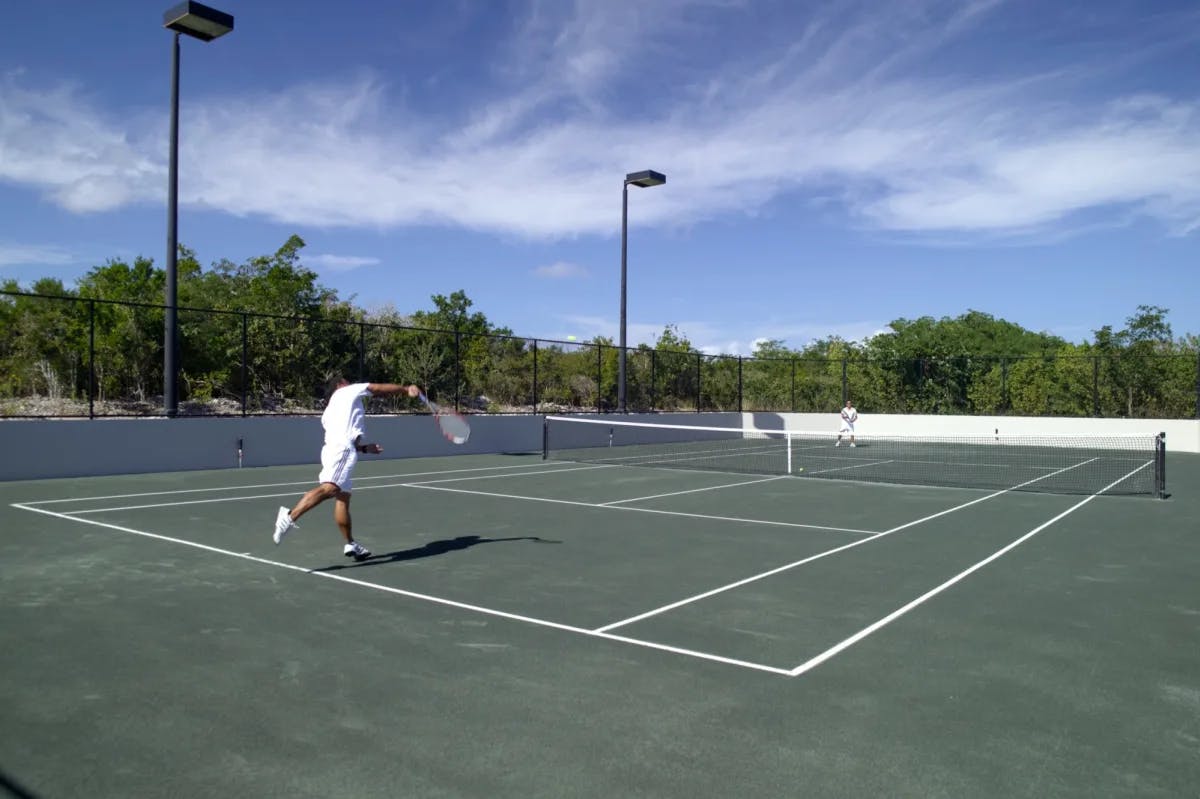 people in white clothing play tennis on a green court