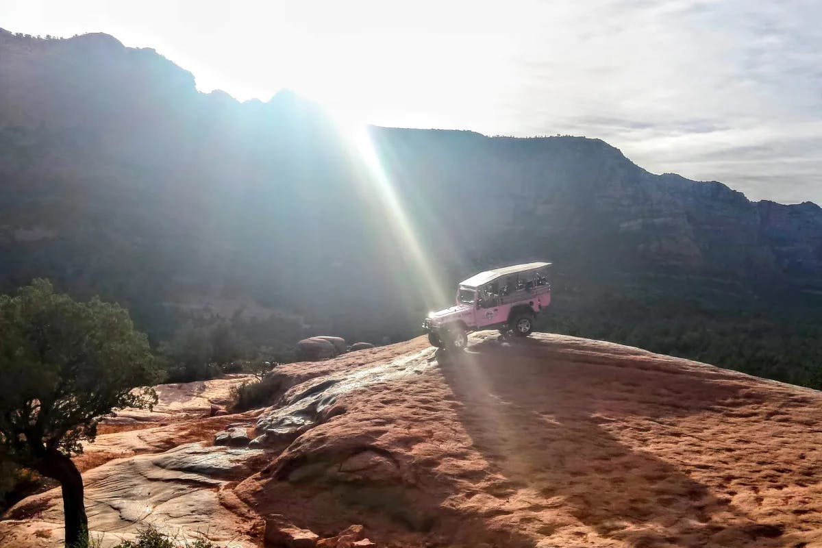 A picture of a pink Jeep parked on a brown mountain during daytime.