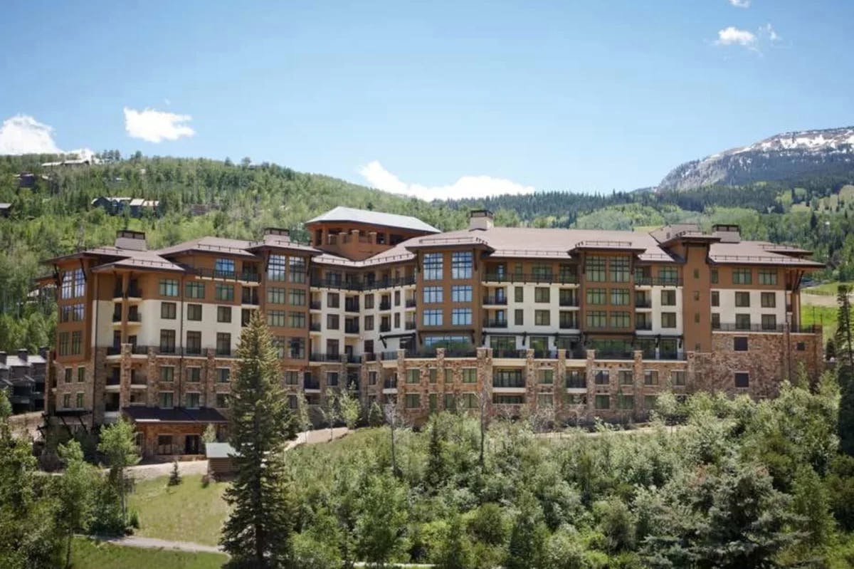 lodge exterior in summertime with green landscape and snowy mountains in the background