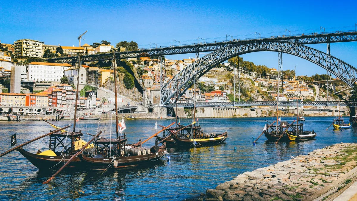 A front row view of Ponte Luis bridge and small, local, wooden boats in the clear, blue water, on a sunny day.