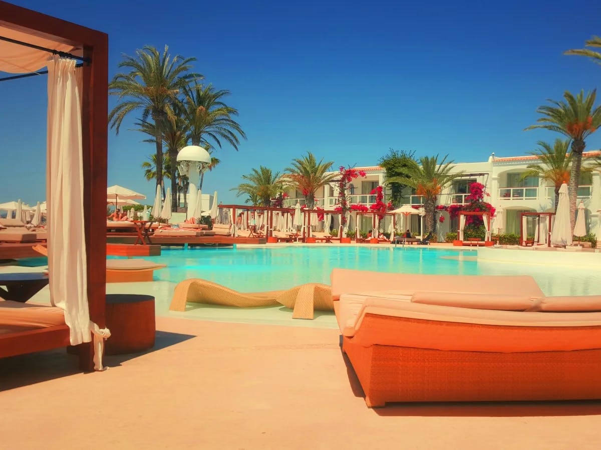 A pool area during the daytime with orange day beds and palm trees around