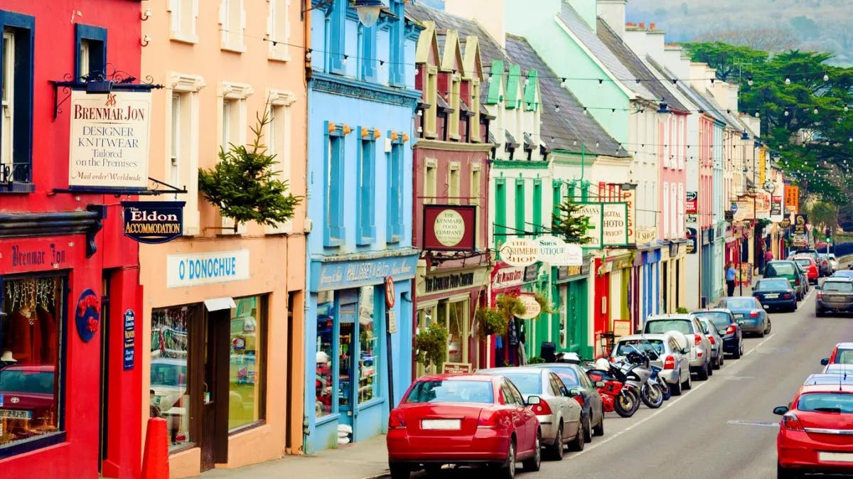 Cars parked on the road with colorful shops on the whole left side of the road