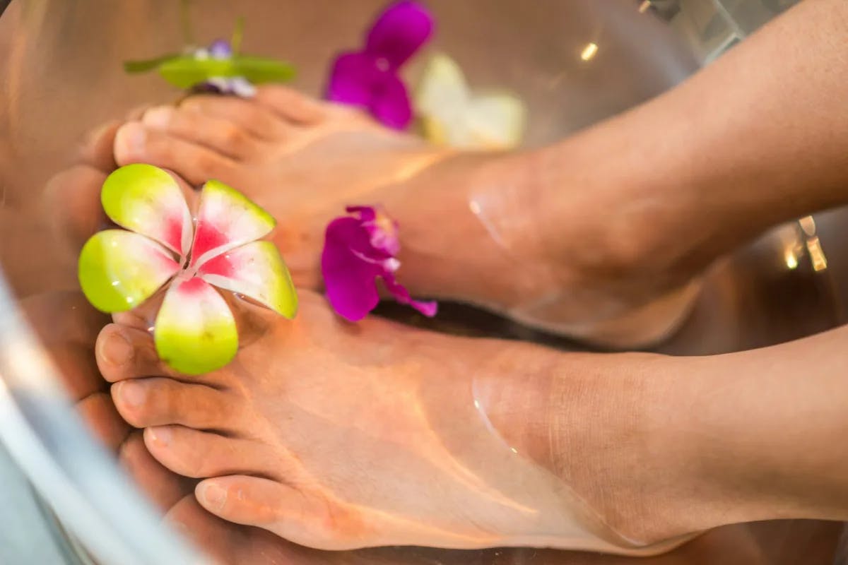 Person's feet soaked in water with flowers.