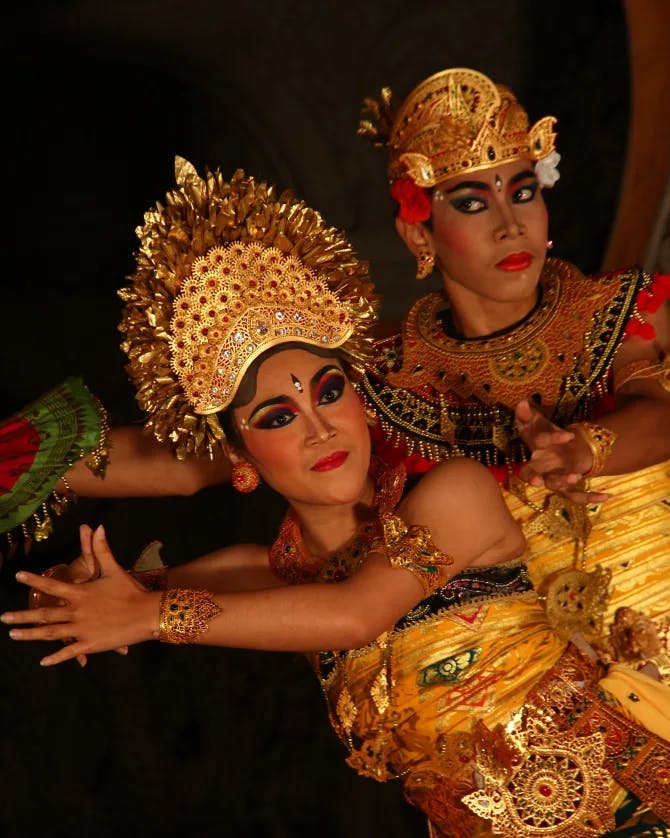 Woman and man dressed in ornate gold traditional Balinese clothing performing a dance.