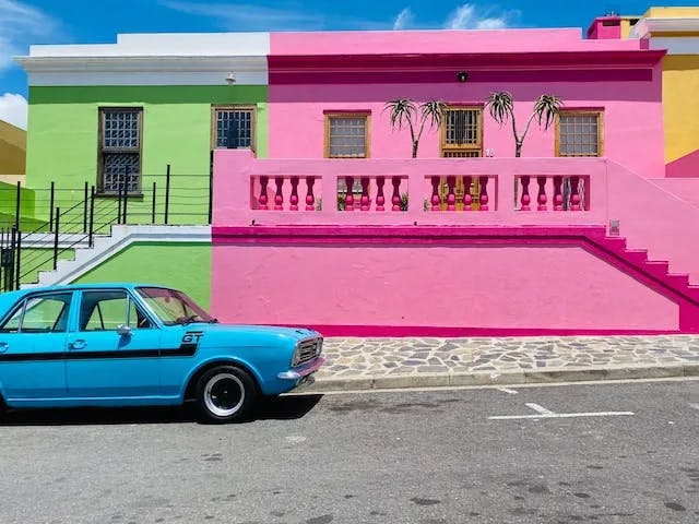 A bright green and pink house with a blue car out front