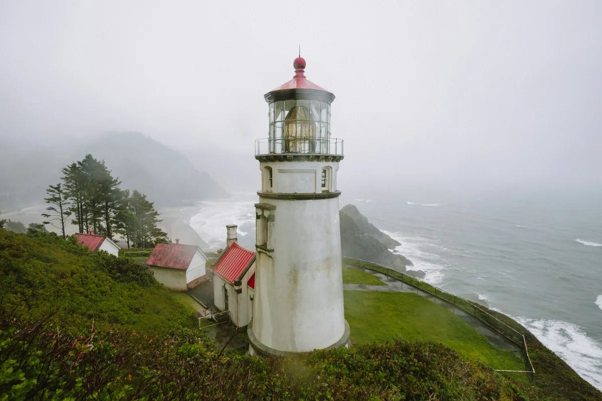 A picture of a lighthouse on top of a lush green hillside during the daytime with a foggy sky