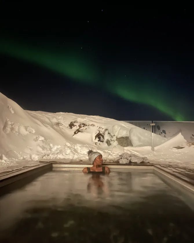 Yasmir relaxing in a hot tub at nighttime under the northern lights