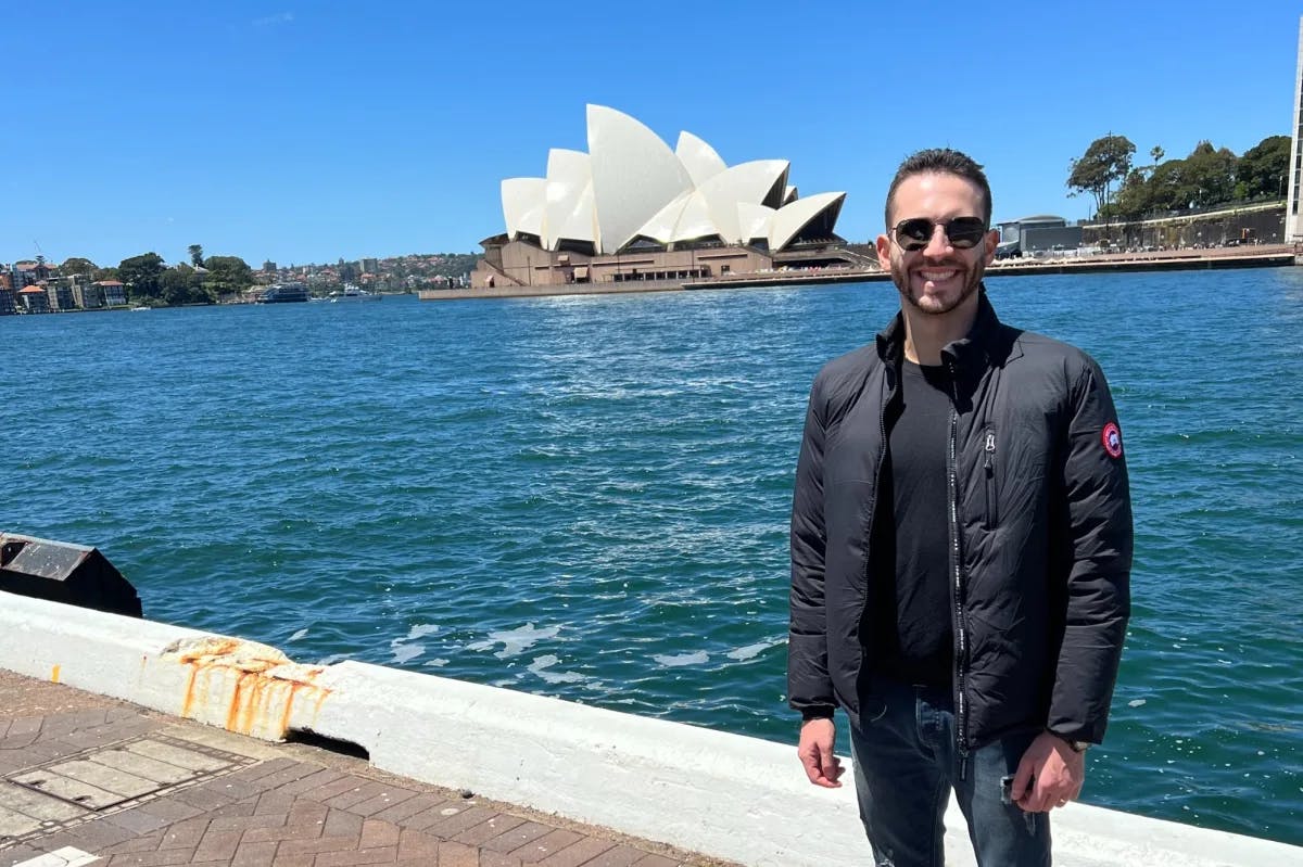 a man stand in front of a harbor with the Sydney Opera House in the distance