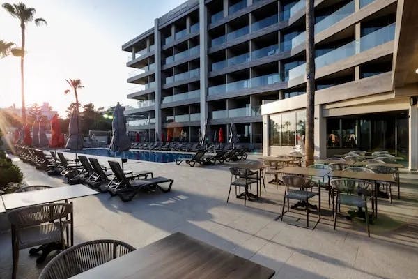 Outdoor dining area of a hotel poolside as the sun sets in the distance. 