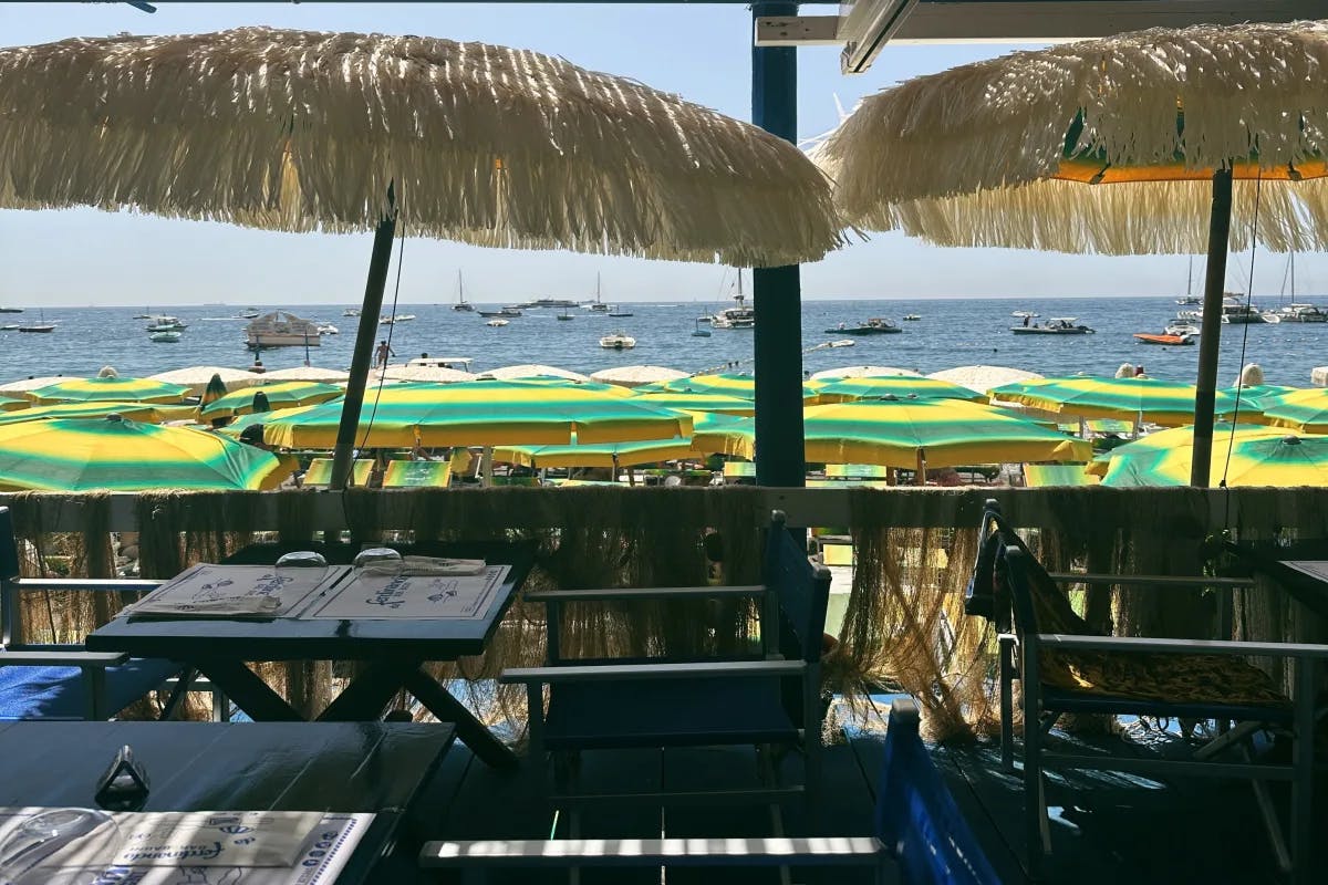 A picture of a beachfront restaurant on a deck with wooden tables and chairs, and many yellow and green umbrellas on the beach in front