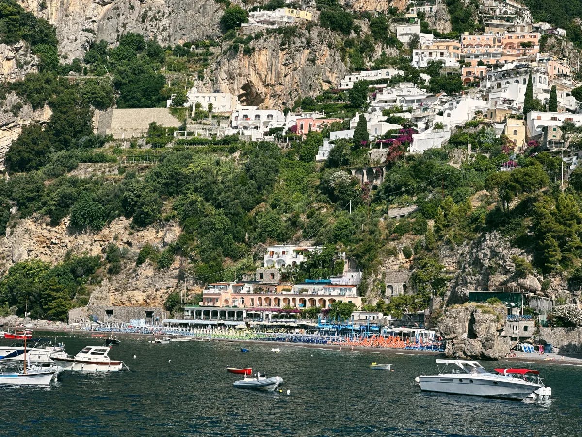 A view of a typical beach club from the ocean with many yachts sailing and buildings built into the cliffside