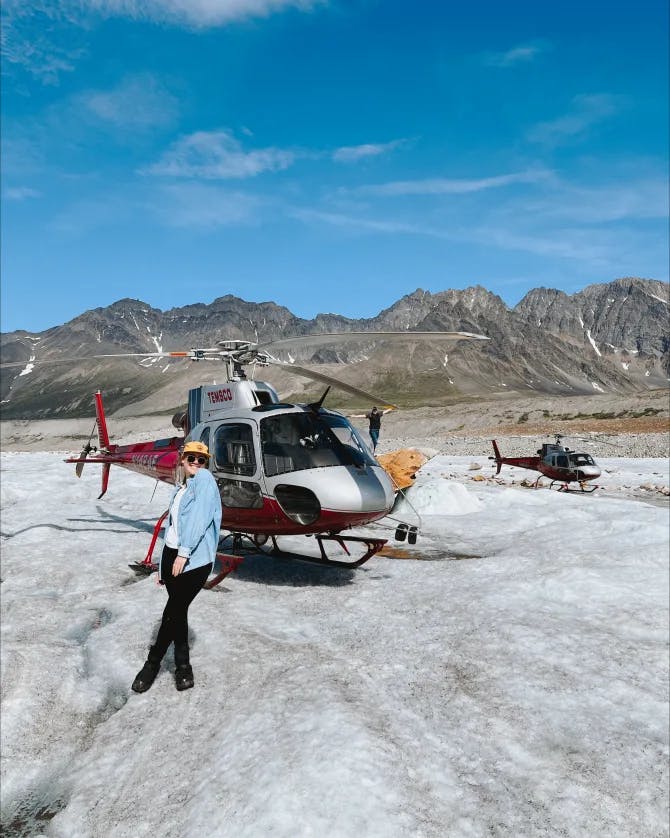 Picture of Maddi standing in front of a landed helicopter with mountains in the background