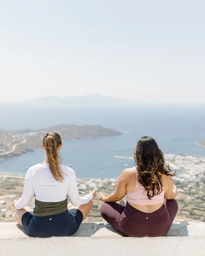 Advisor sitting on a look out point with her friend gazing out at a view with a city in the distance.