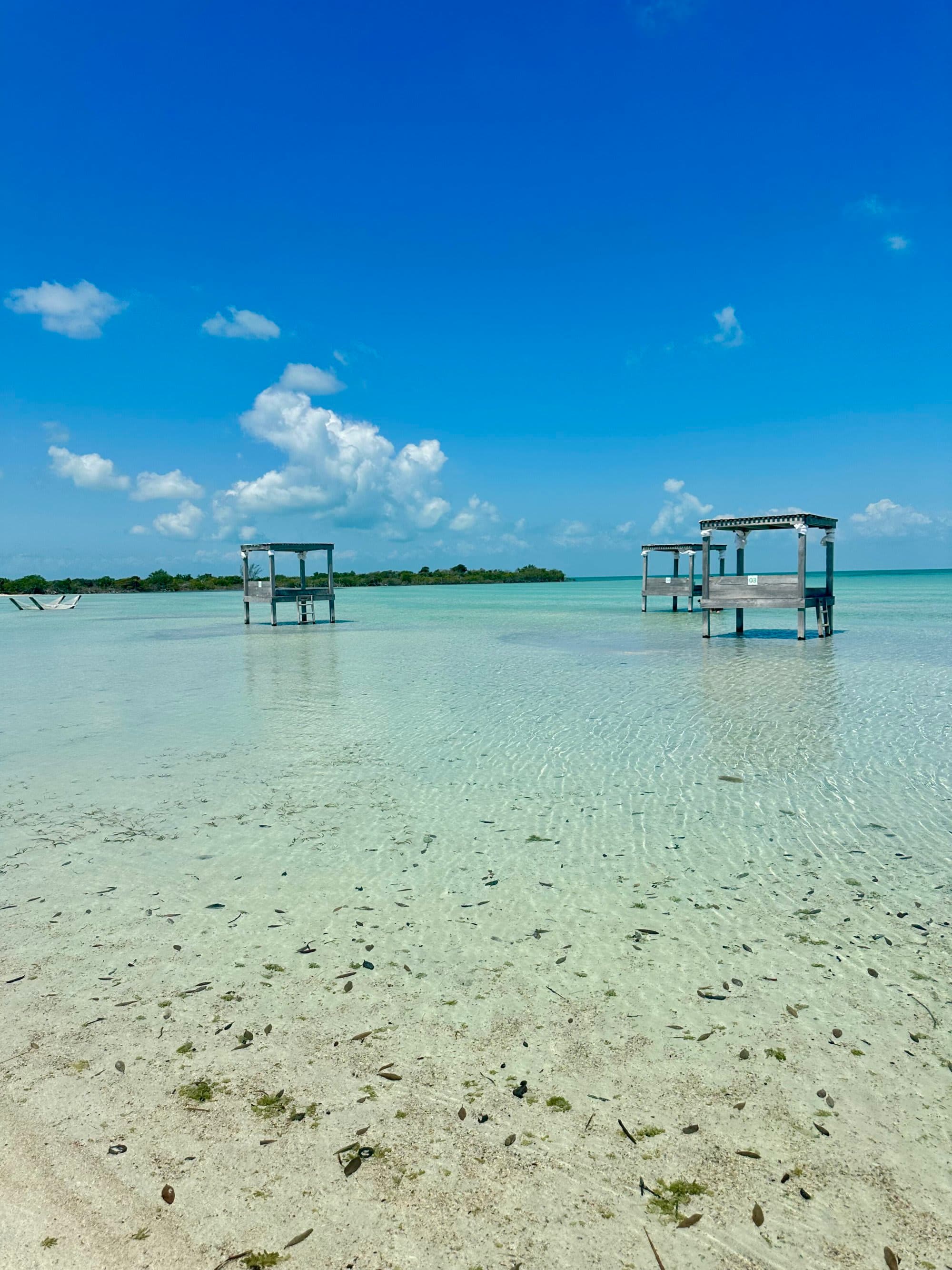 A clear shallow body of water with two dilapidated wooden structures under a blue sky.