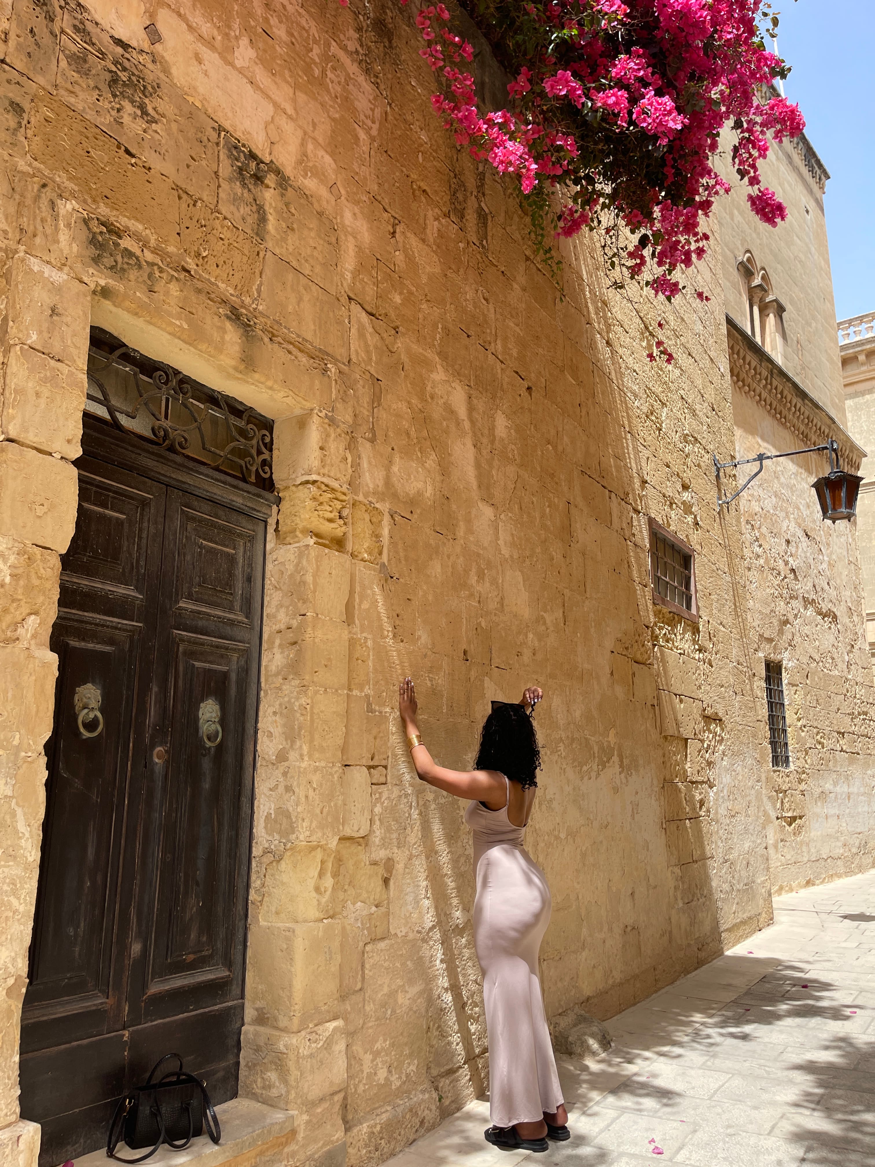 Advisor touching an old stone wall on a sunny street with pink flowers overhead