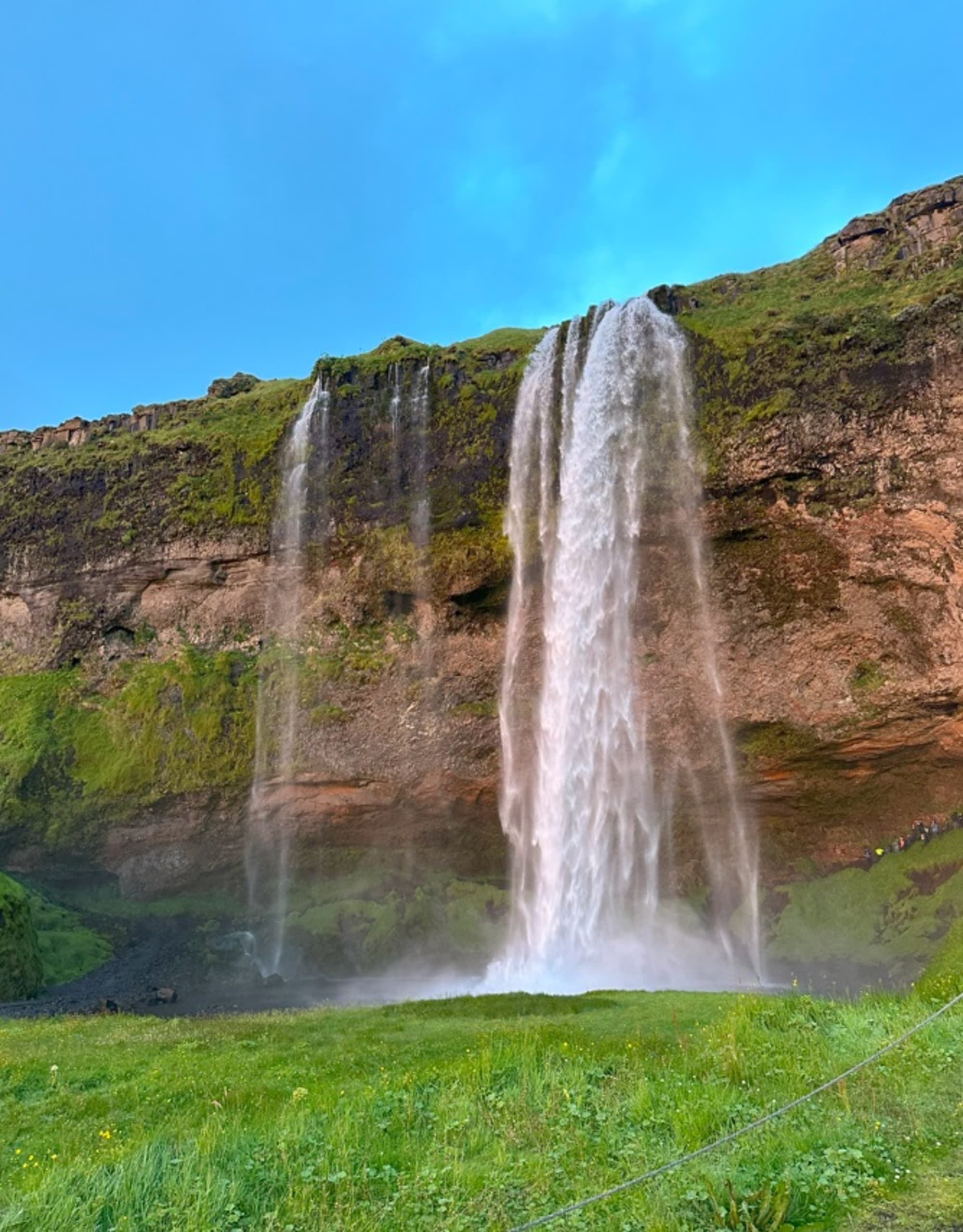 A majestic waterfall cascading down a lush, green cliff under a clear blue sky.