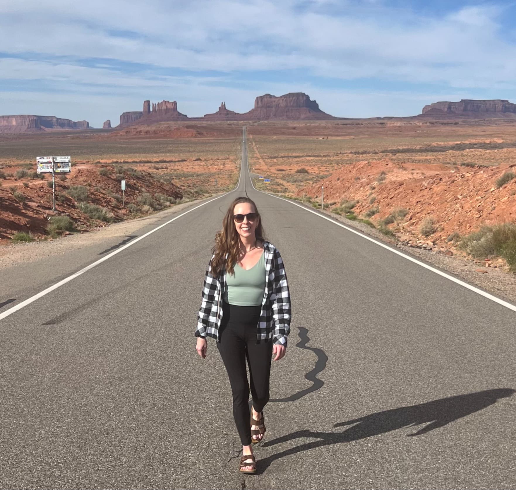 The advisor walks down the median line of a two-lane highway with desert formations in the background.