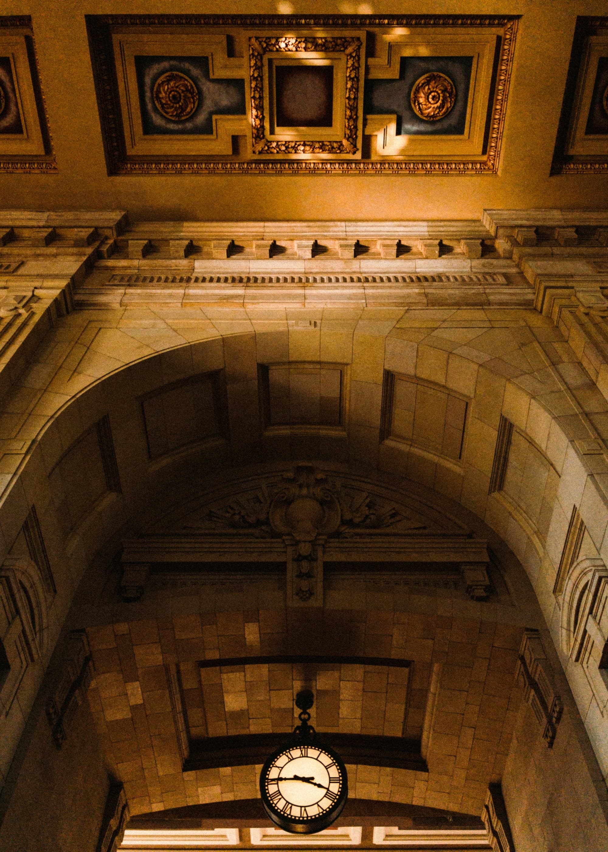 An ornate ceiling with intricate moldings, a hanging clock and framed artwork