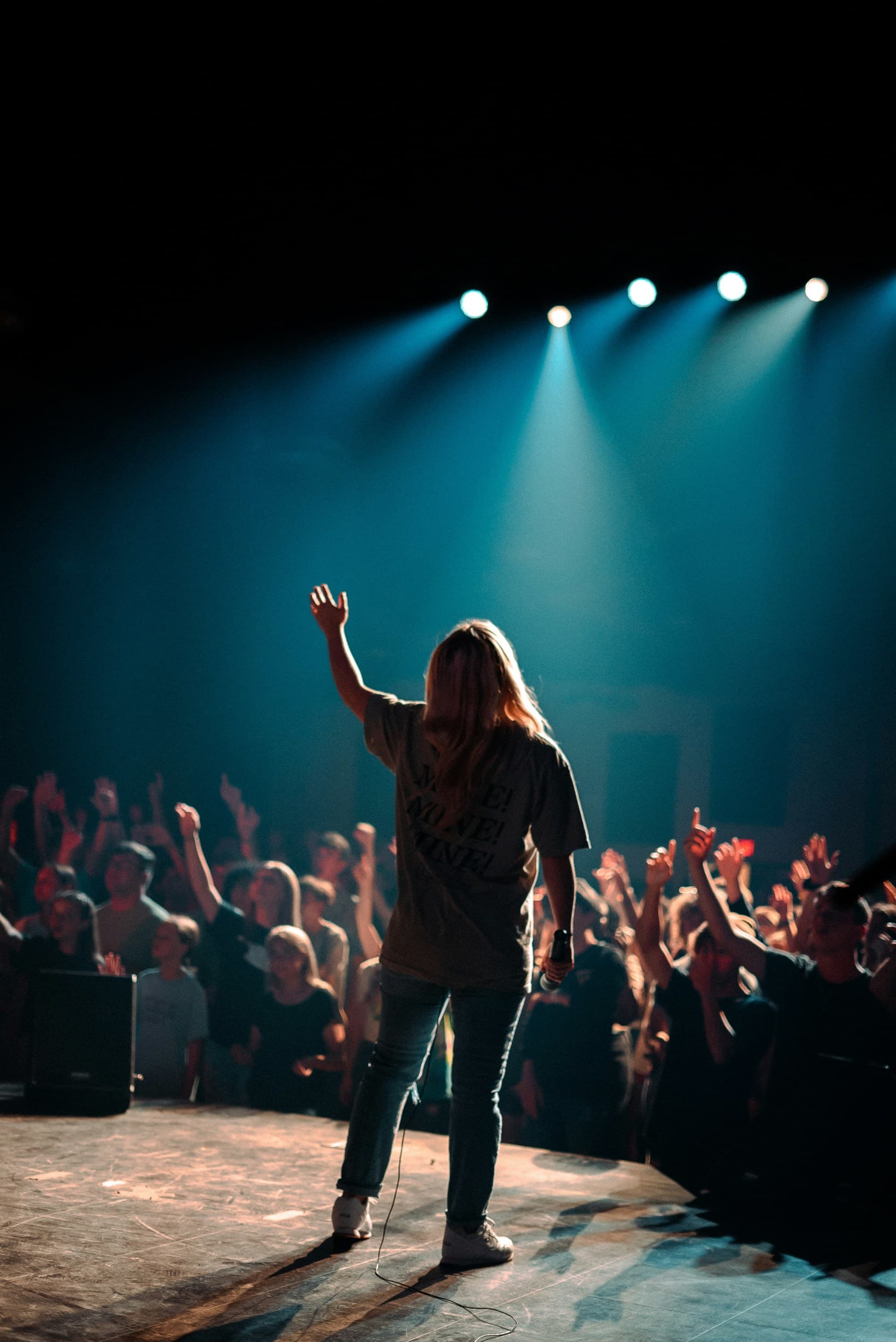 A person on stage faces a crowd under blue stage lights, capturing a moment of live performance and audience engagement.