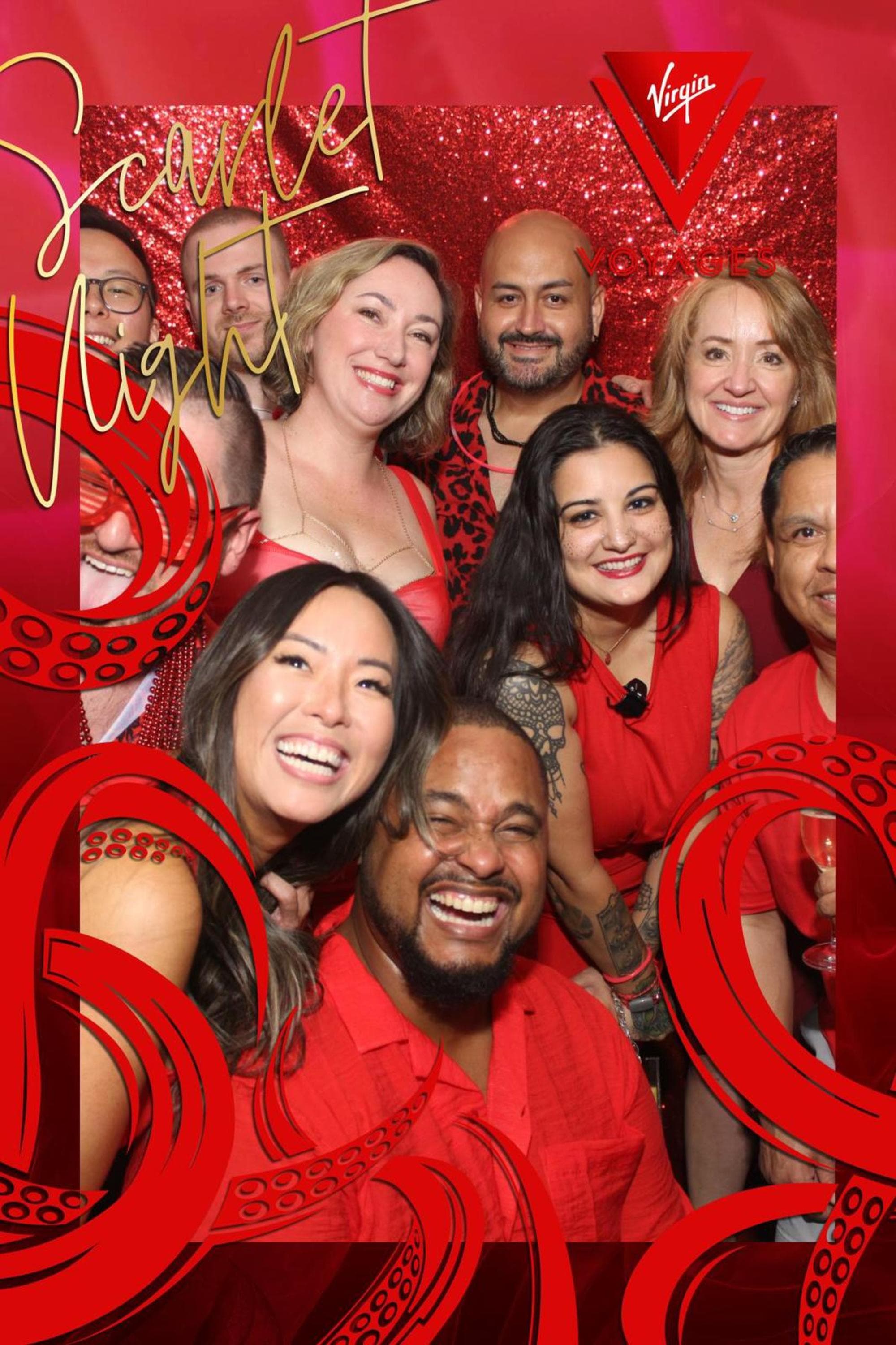 A group of smiling people dressed in red poses against a glittering red backdrop for a "Scarlet Night" event hosted by Virgin Voyages.