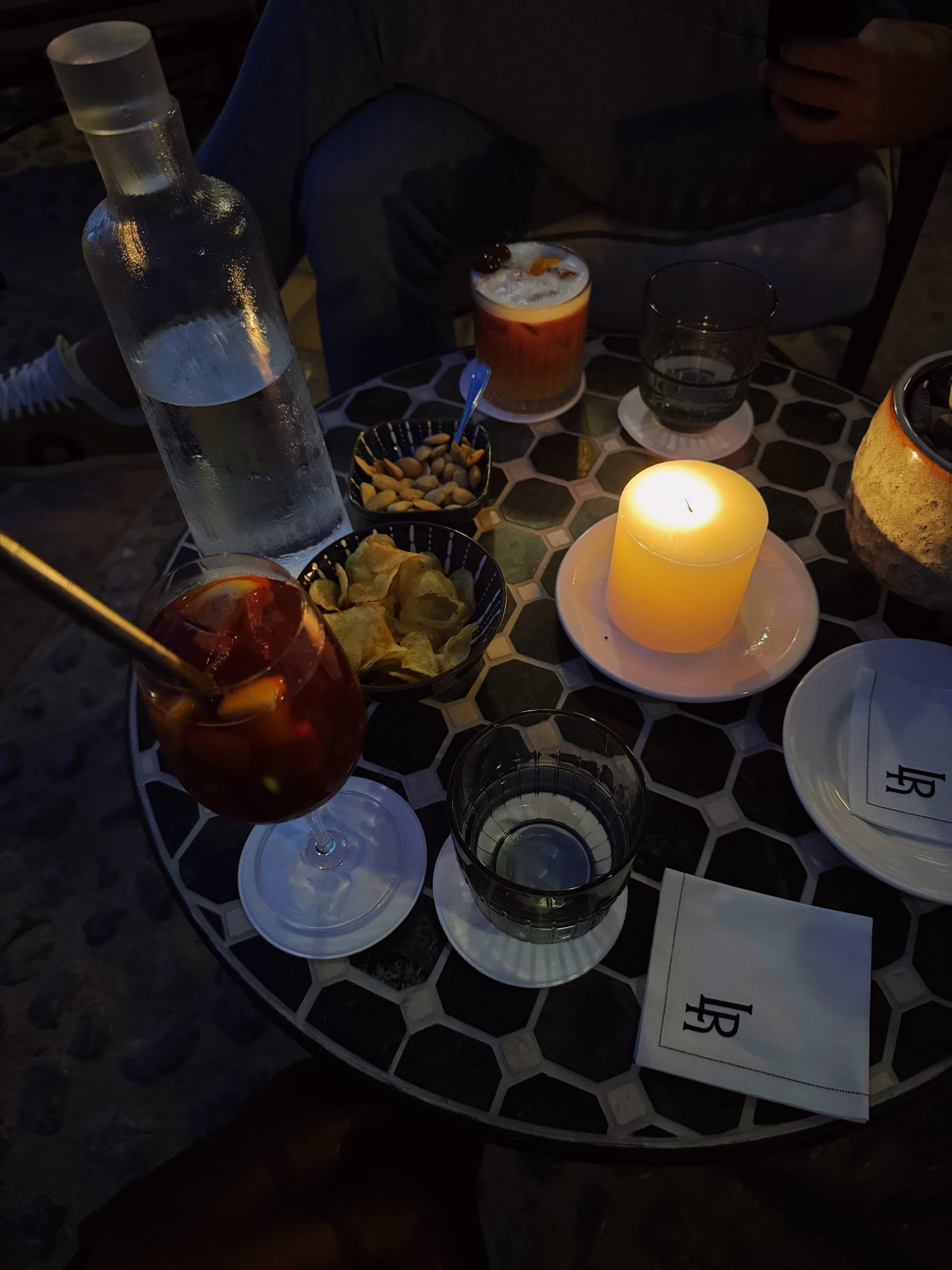 A table set with various drinks and snacks, illuminated by candlelight for an intimate atmosphere.