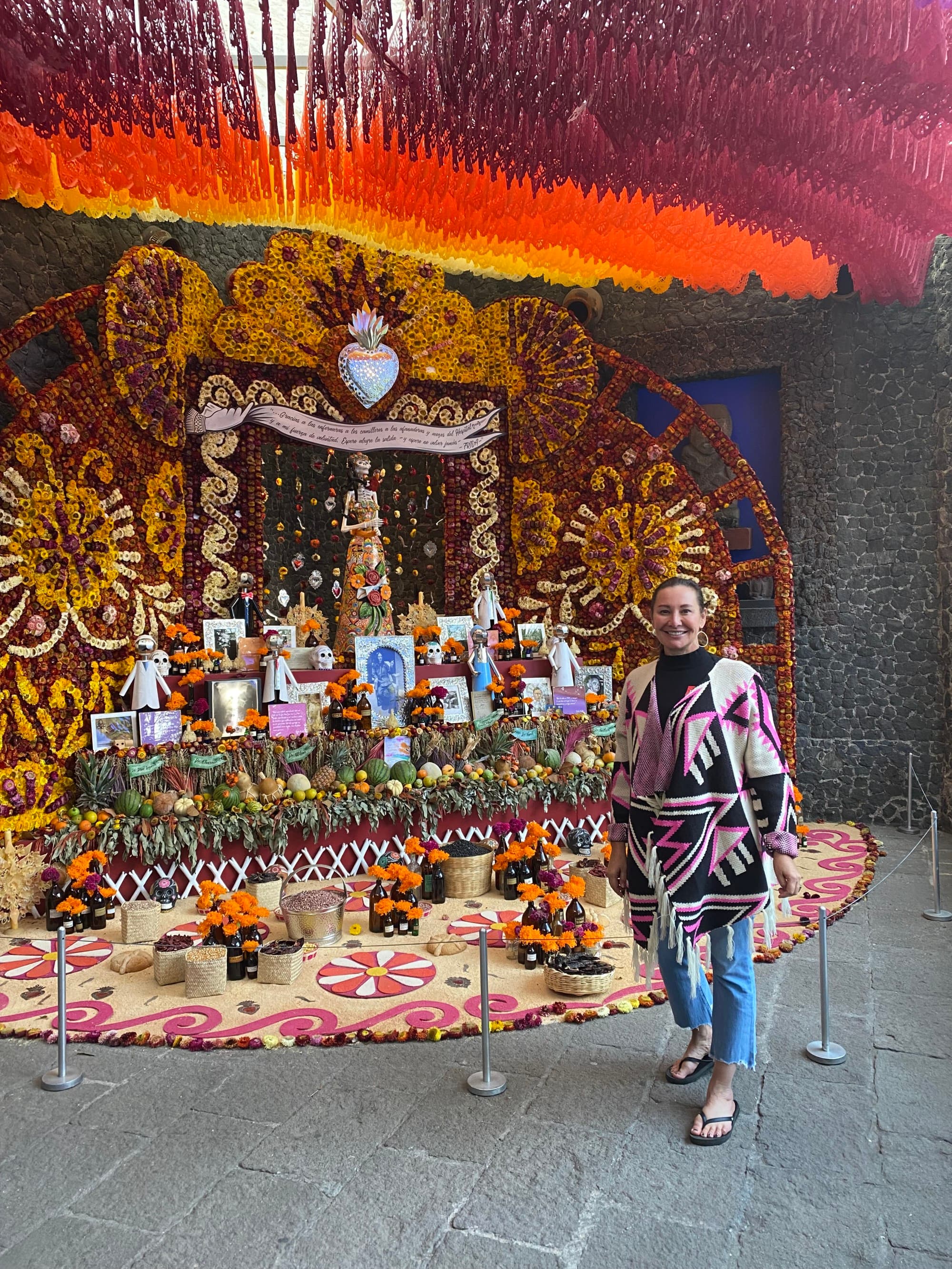 A woman standing besides a colorful decorated altar with traditional flowers and decorations in Mexico City.