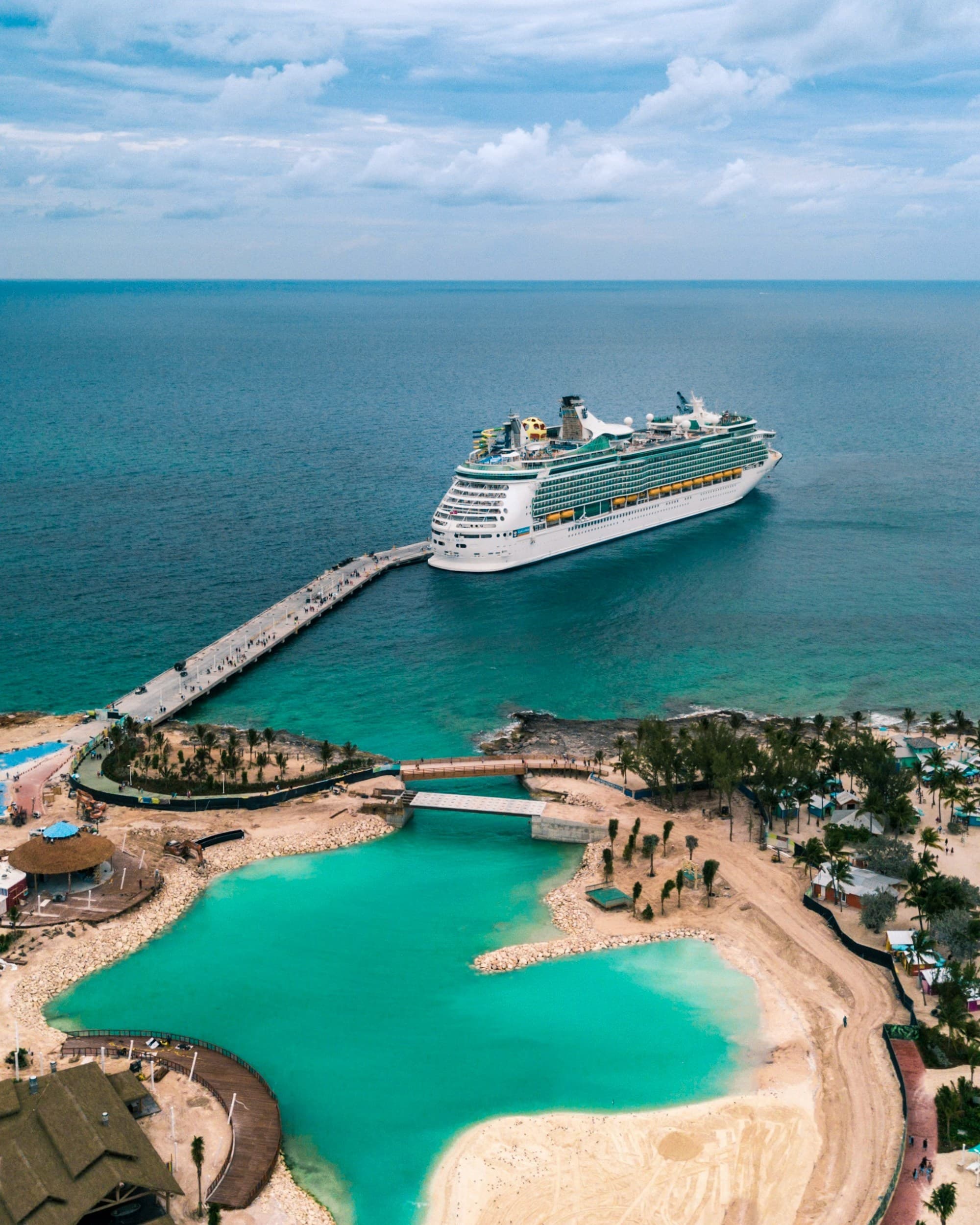 A majestic cruise ship is docked at a pier, surrounded by a serene turquoise lagoon and lush palm trees.