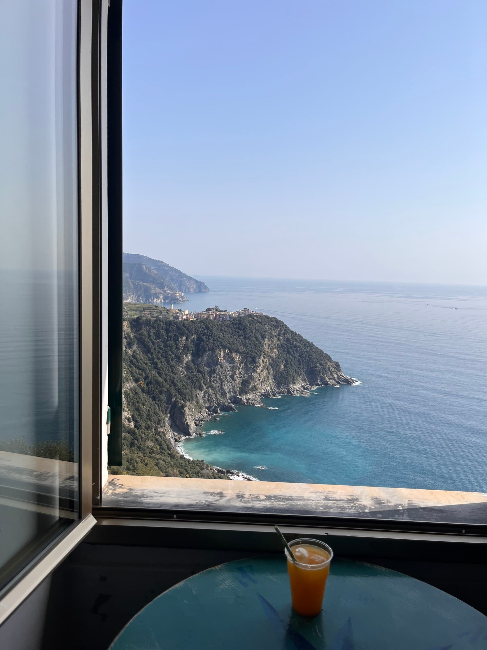 Orange juice on a table by the window with a view of the ocean as waves lap the rocky shore.