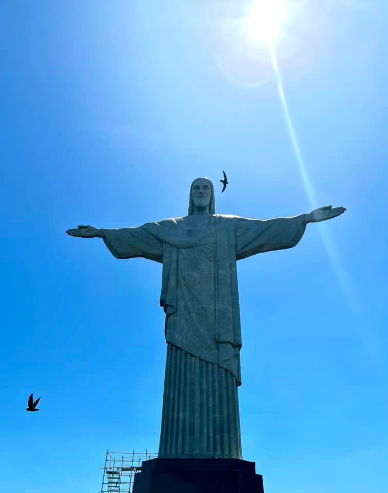 Grey statue of a man with open arms on a sunny day.