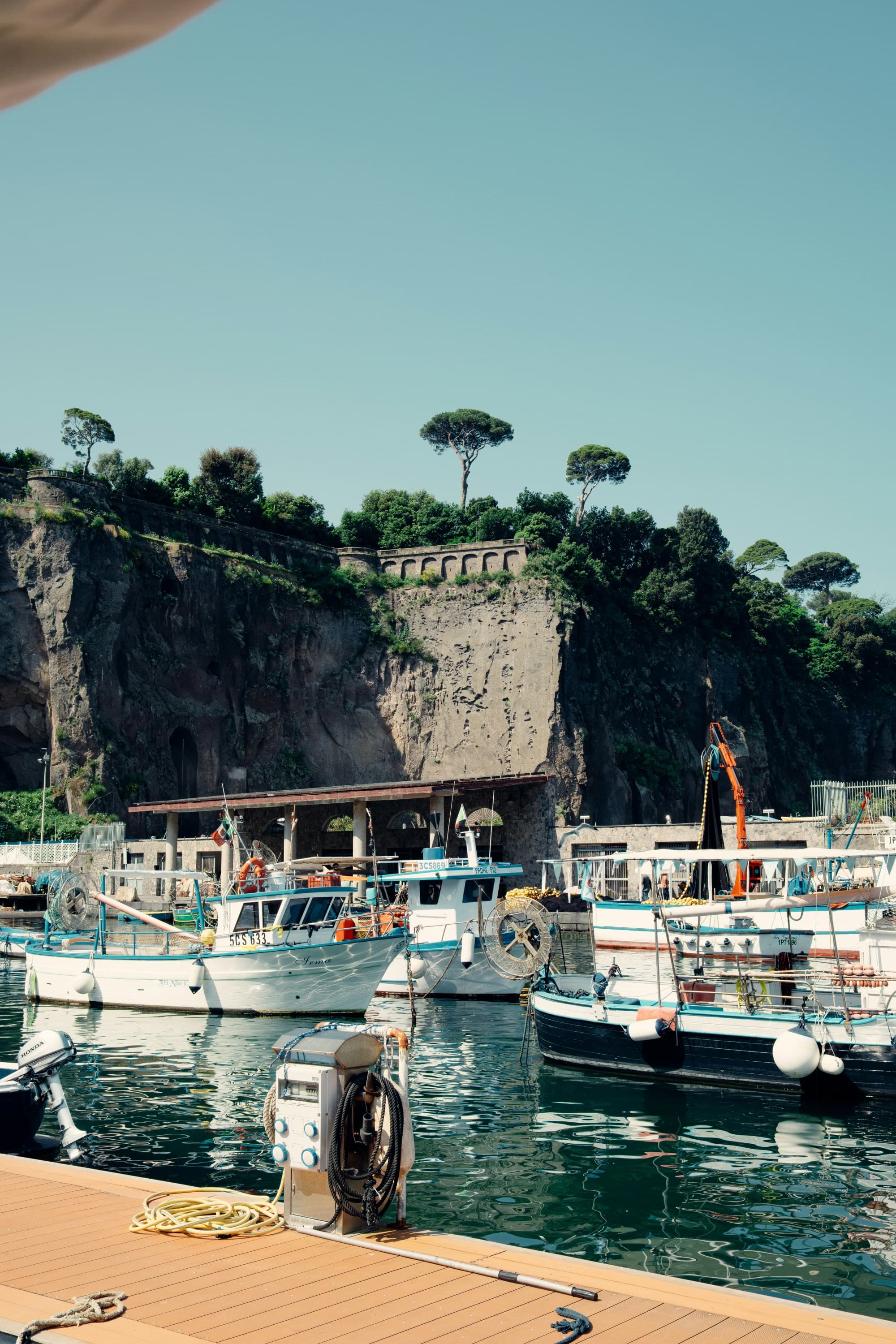 A scenic harbor with boats and a cliff adorned with trees in the background.